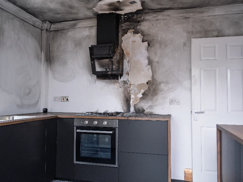 Kitchen corner with black cabinets and oven, showing extensive fire and smoke damage on walls and ceiling. fire damage restoration