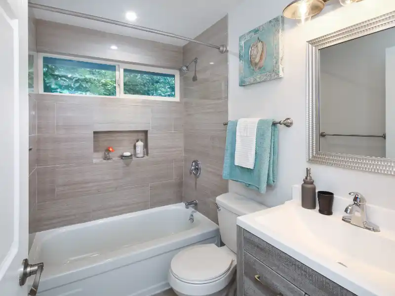 Modern bathroom with a bathtub, toilet, sink, and teal towels hanging on a rack. sewage cleanup services