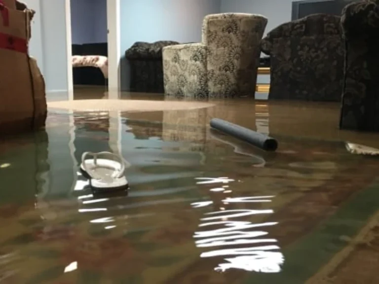 Living room floor flooded with water, a single white flip-flop and a pipe floating. flood damage restoration